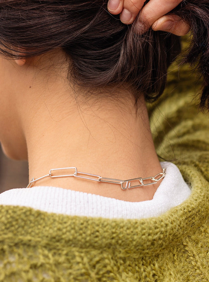 Silver necklace with rectangular links and decorative orbit feature.